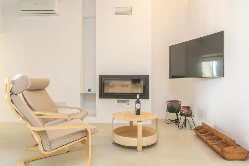 Una sala luminosa con asientos reclinables, una mesa de centro redonda y un televisor en la pared.