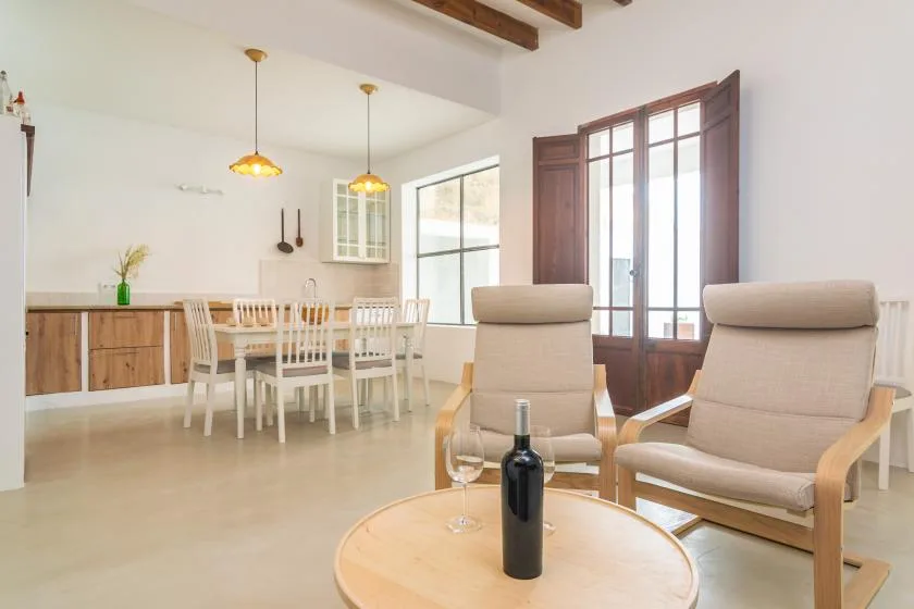 Un luminoso espacio de comedor y estar con una mesa de madera y dos sillones.