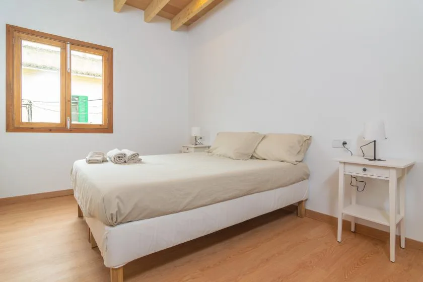 Un dormitorio con una cama doble, mesitas de noche y una ventana con marco de madera.