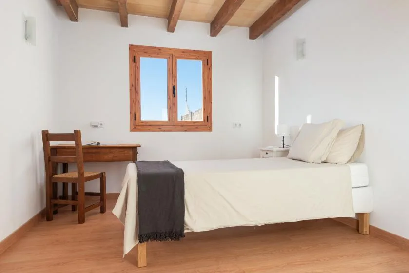 Un dormitorio luminoso con una cama y un escritorio de madera junto a una ventana.