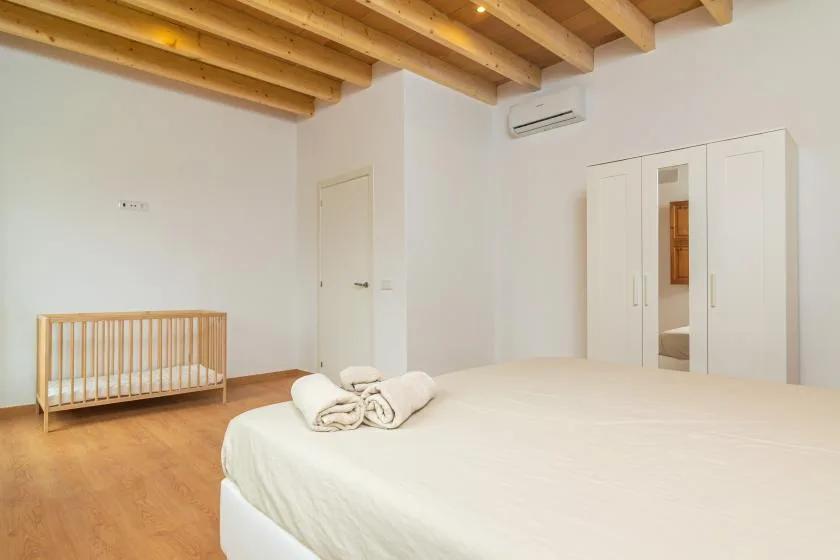 Un dormitorio luminoso con una cama grande, una cuna de madera y vigas de techo a la vista.