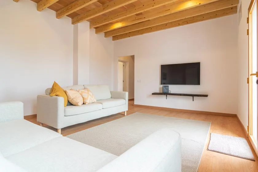 Una sala luminosa con asientos claros y un televisor montado en la pared.