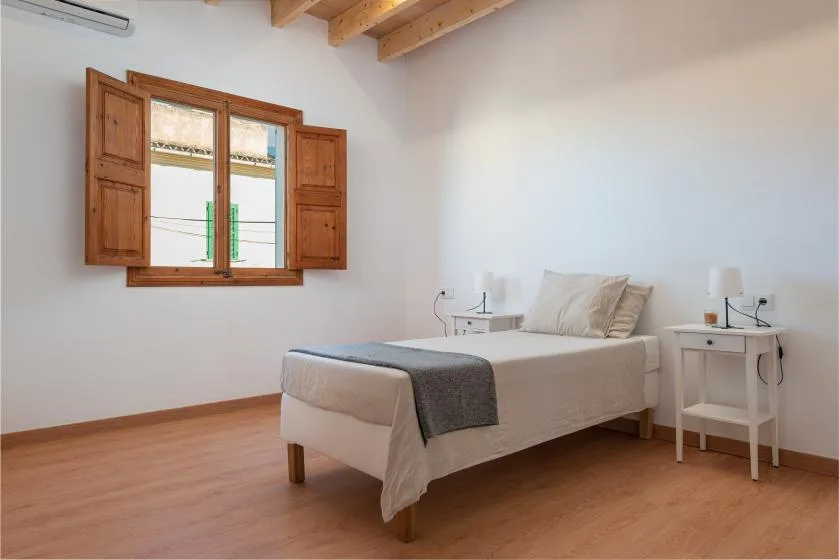 Un dormitorio con una cama, mesitas de noche y una ventana con contraventanas de madera.