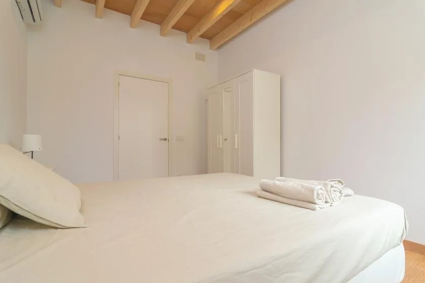Un dormitorio luminoso con una cama, toallas dobladas y un armario.