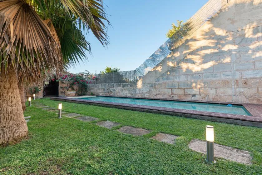 Una piscina estrecha bordea un jardín de césped y un muro de piedra.
