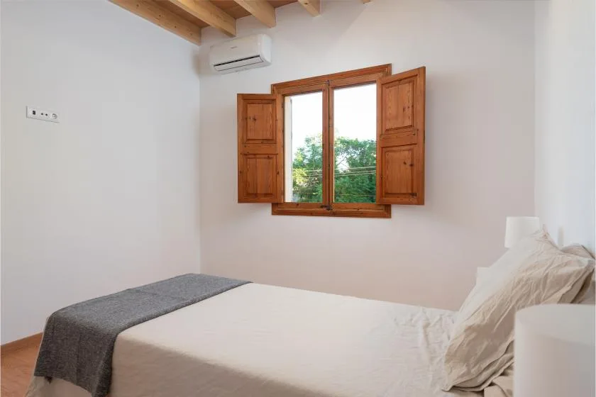 Un dormitorio con una cama bajo una ventana de madera abierta.