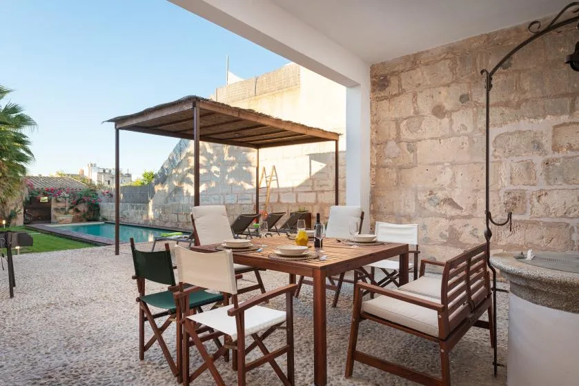 Una zona de comedor al aire libre con mesa y asientos junto a una piscina.