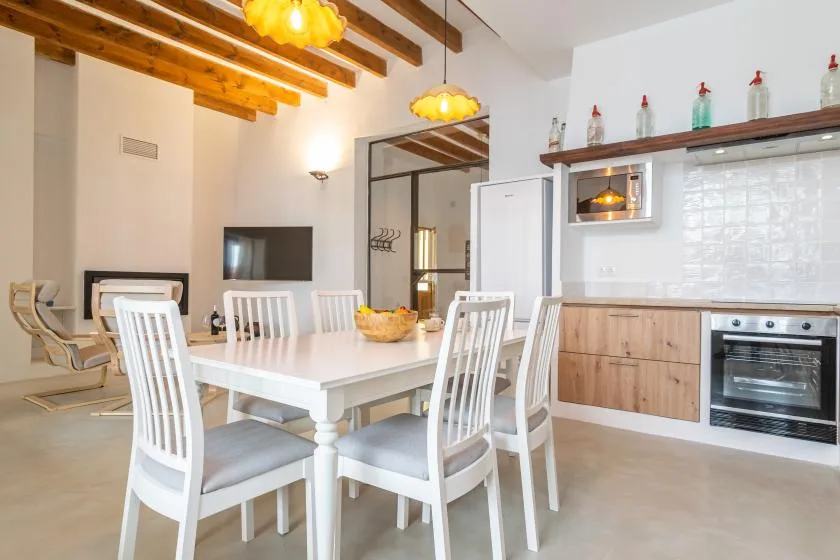 Un comedor luminoso con asientos blancos y una cocina contigua.