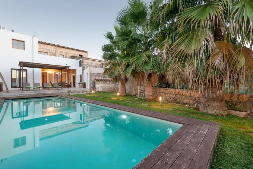 Una piscina junto a un edificio moderno, con palmeras junto al muro del jardín.