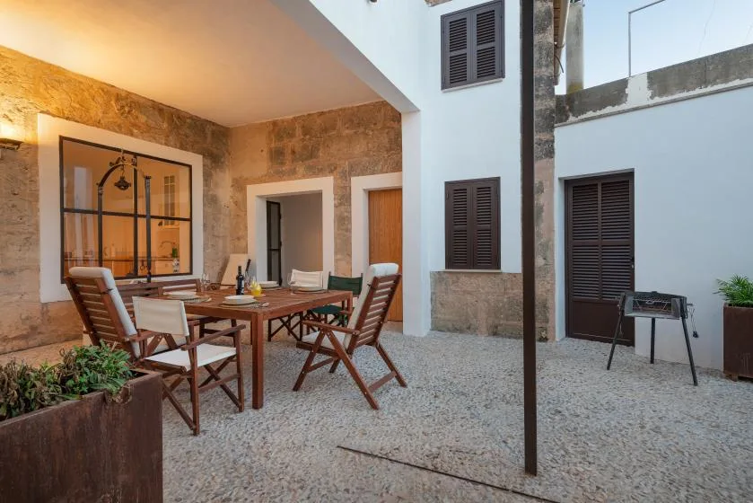 Una zona de comedor al aire libre con mesa de madera y asientos en un patio de piedra.