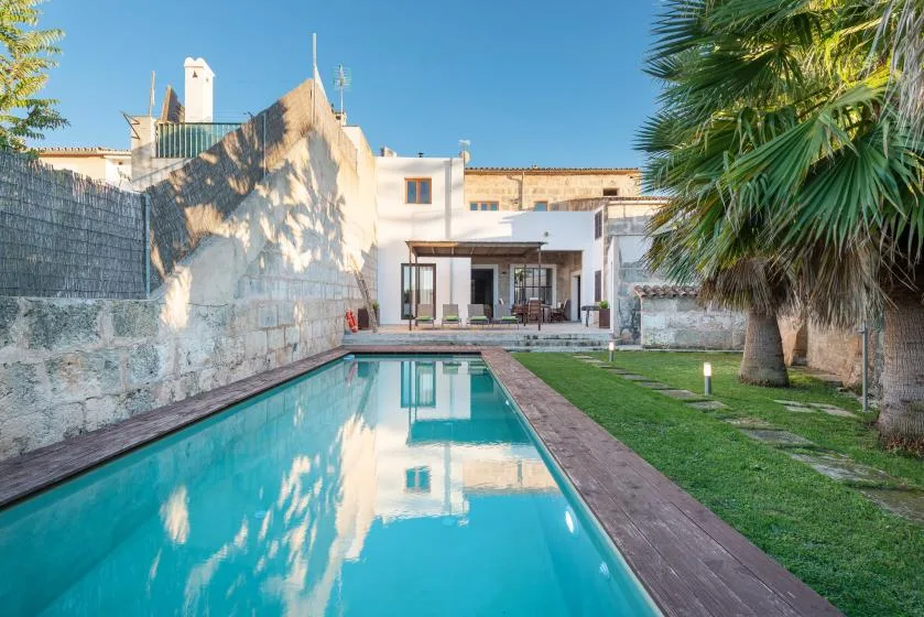Una piscina y un jardín con césped conducen hacia un edificio blanco.