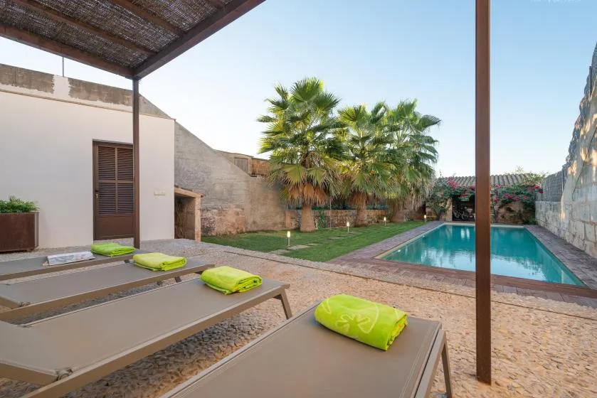 Un patio junto a la piscina con asientos reclinables y palmeras.