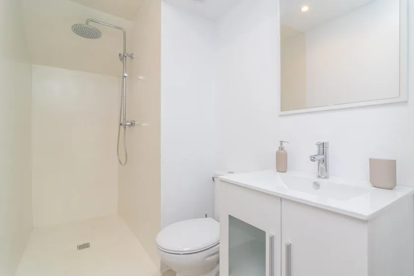 Un baño luminoso con ducha, inodoro y tocador con lavabo.