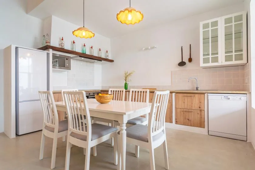 Una cocina luminosa con un comedor y una mesa larga con sillas blancas.