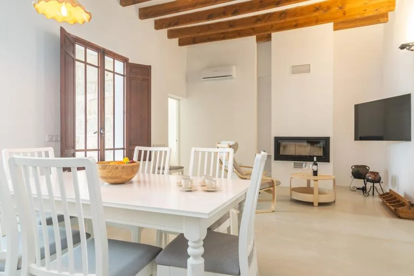 Un comedor y sala de estar luminosos con una mesa blanca y un televisor en la pared.