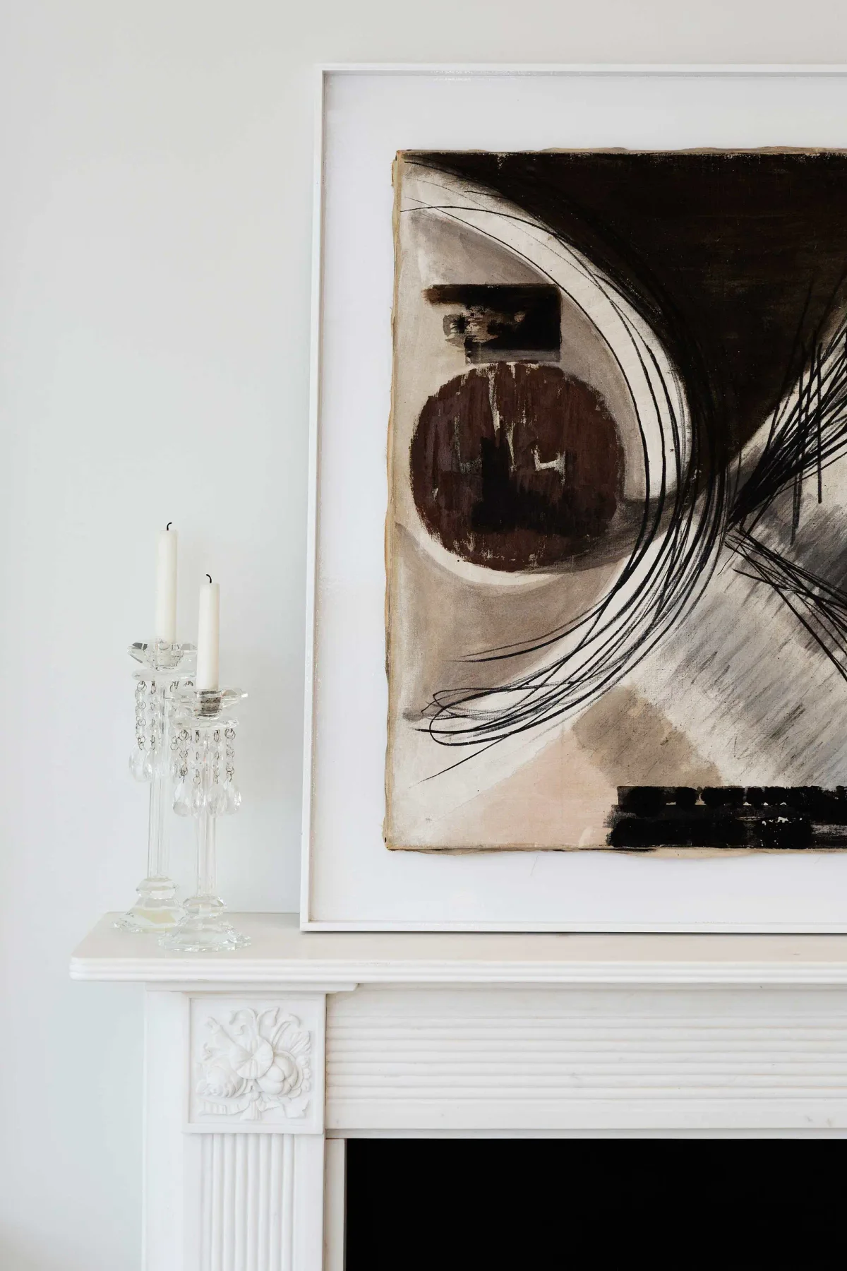 Una obra abstracta cuelga sobre la repisa blanca de una chimenea en un interior luminoso.
