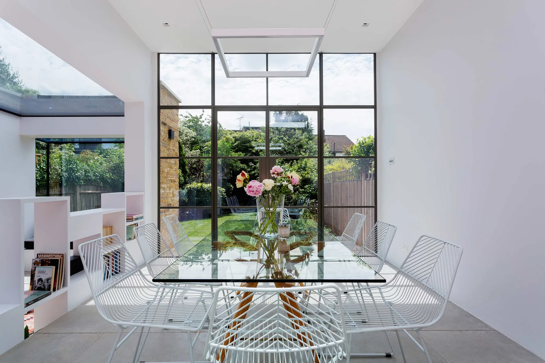 A bright dining area with a glass table and large windows overlooking greenery.