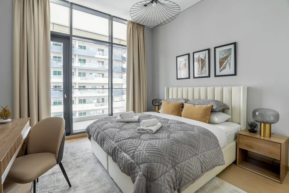 A bedroom with a large bed, gray bedding, and tall windows.