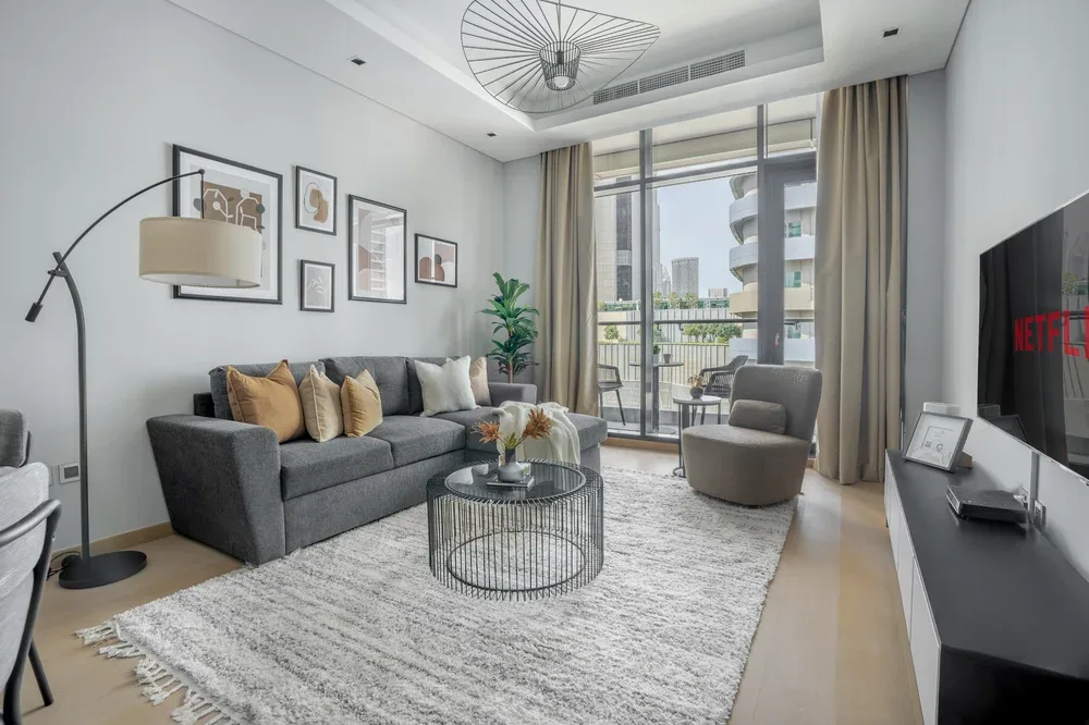 A living room with gray seating, a glass coffee table, and large windows.