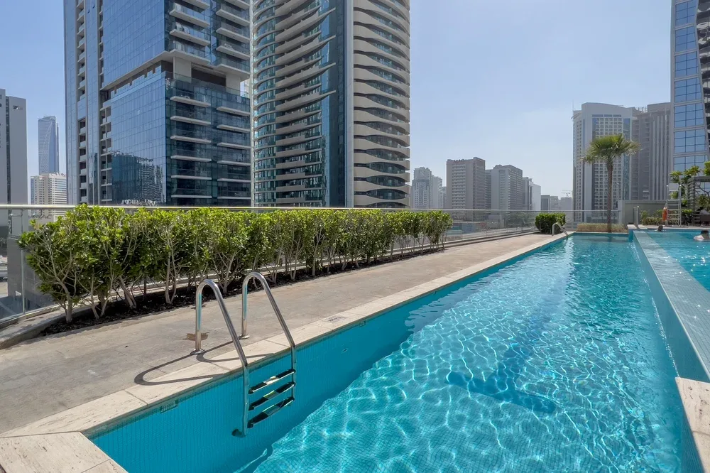 A rooftop swimming pool overlooks a skyline of modern high-rise buildings.