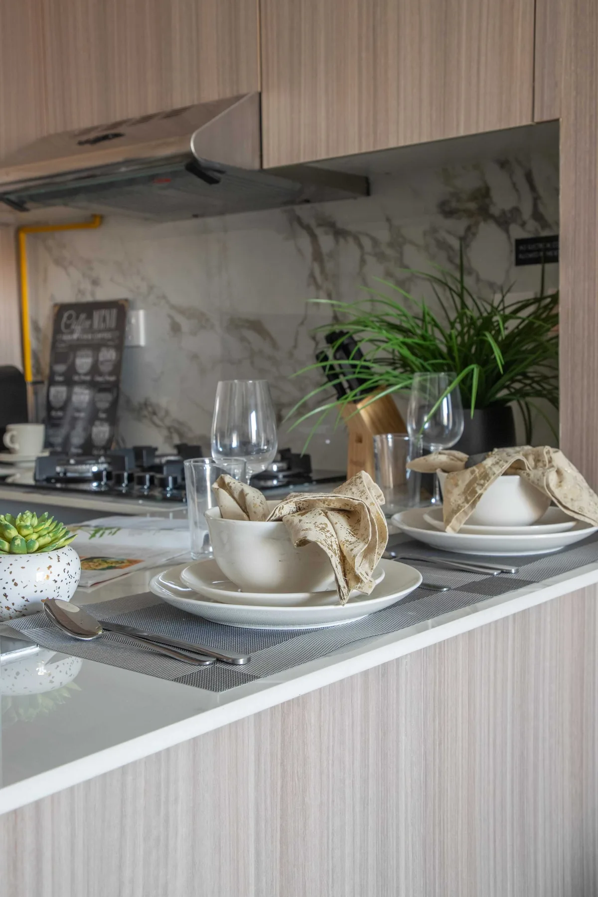 Una barra de comedor está preparada con platos, tazas, copas y una planta.