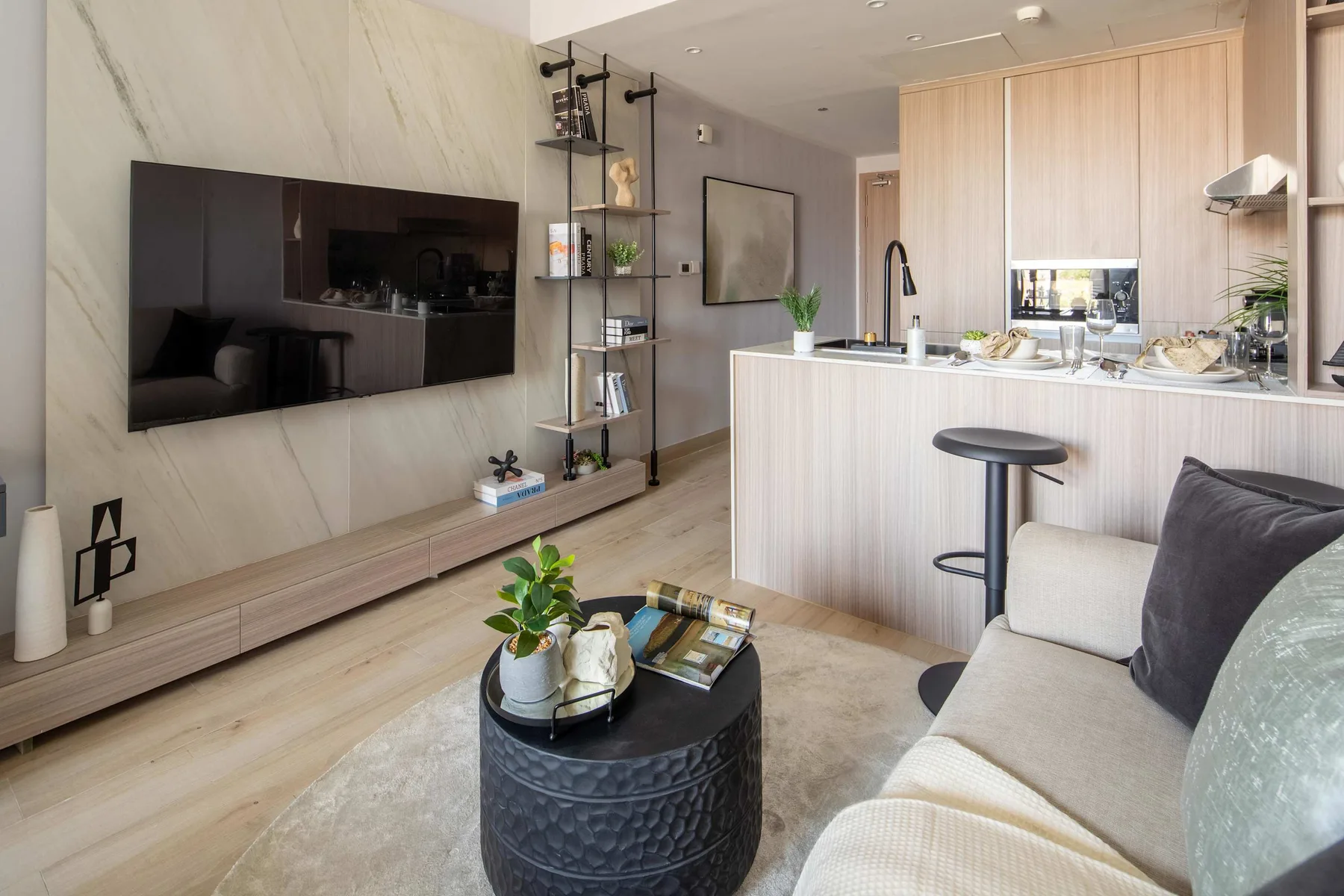 Una sala de estar moderna da a una cocina, con un televisor en la pared y asientos.