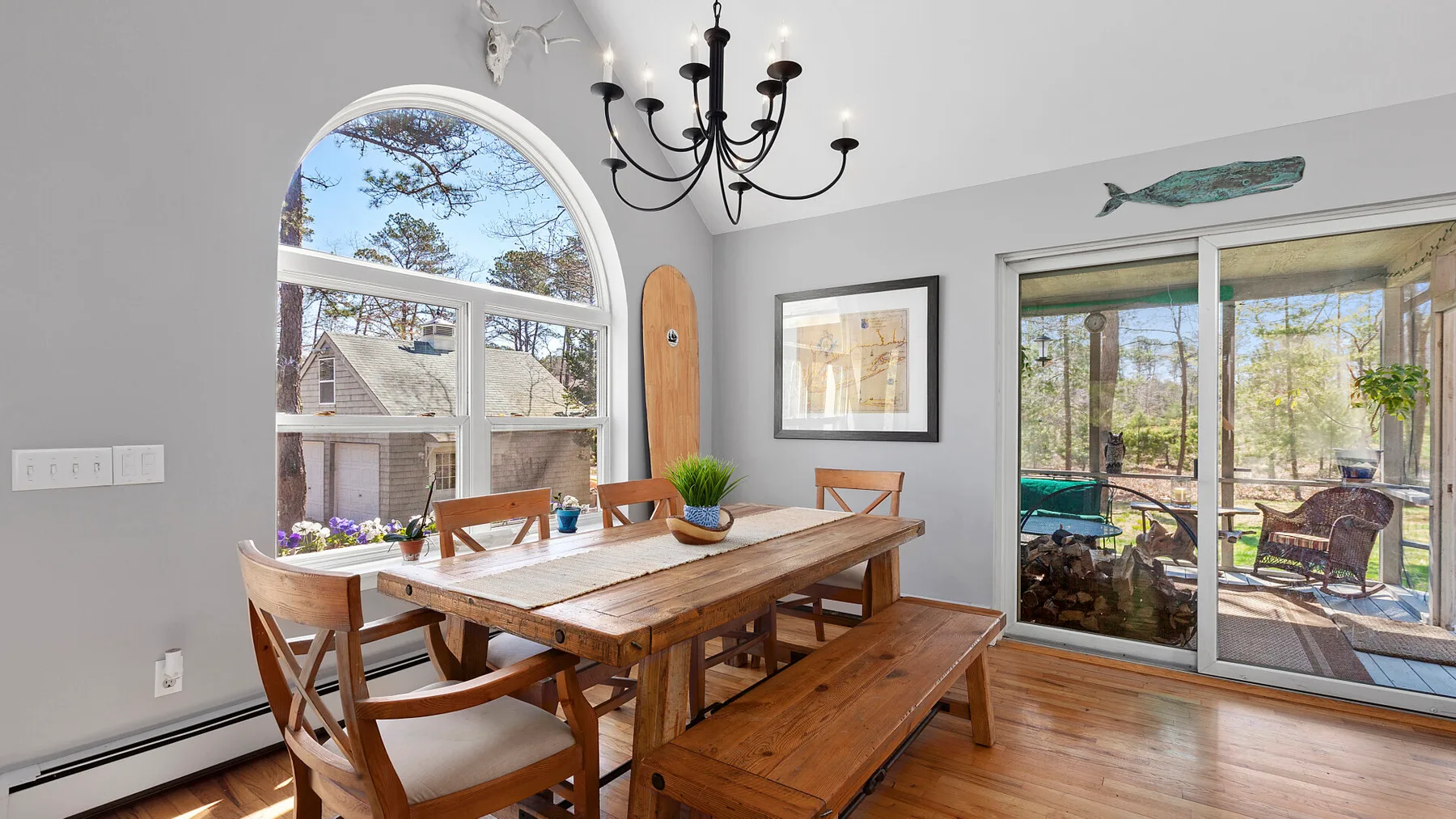 Un comedor con una mesa de madera, una ventana arqueada y puertas de vidrio hacia una terraza.
