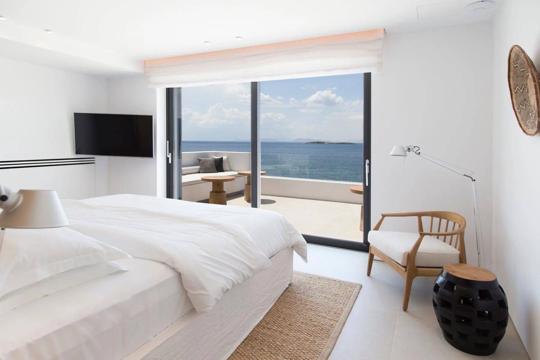 Un dormitorio luminoso con ropa de cama blanca y puertas correderas de cristal frente al mar.