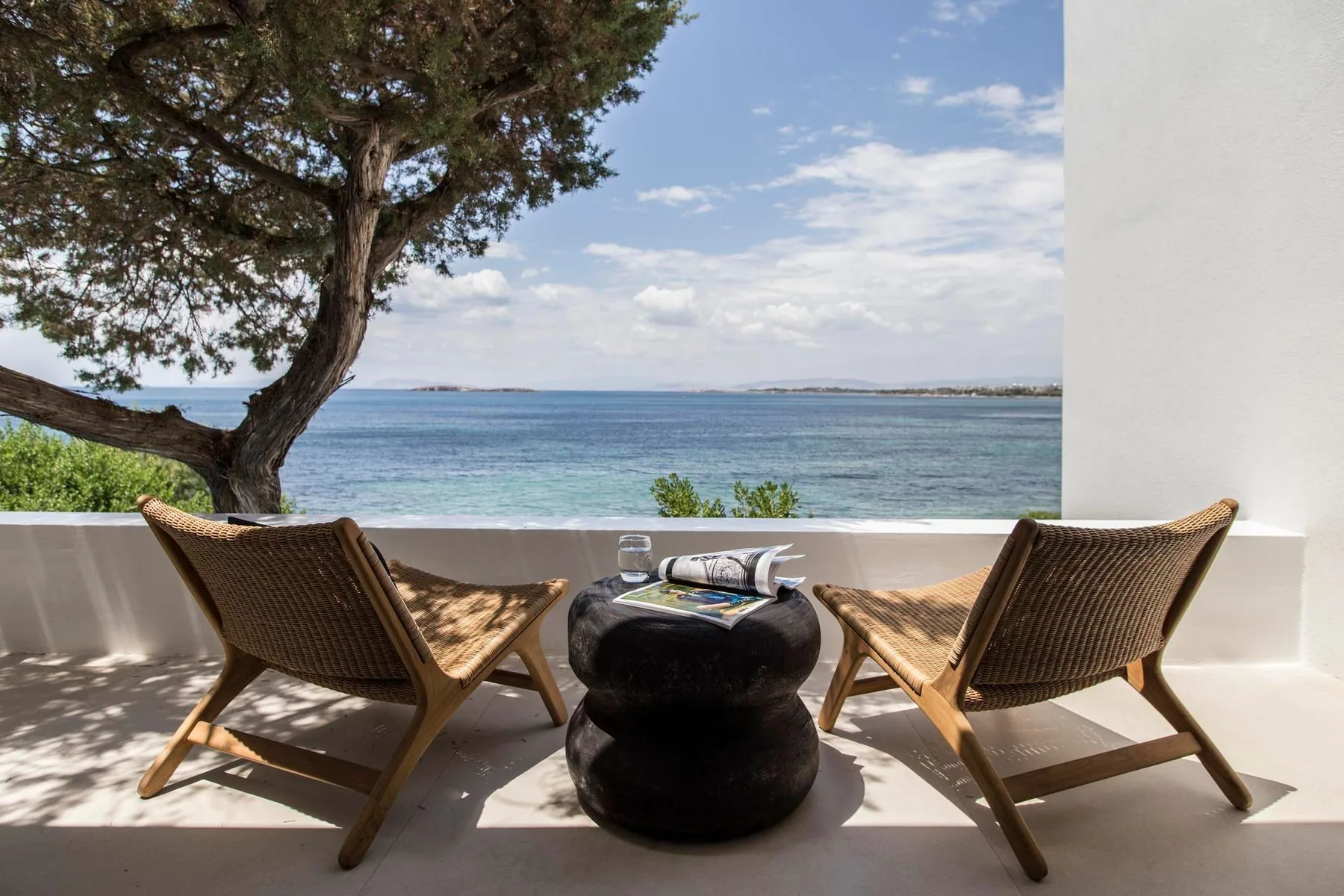 Una terraza junto al mar tiene dos asientos y una mesa pequeña frente al agua.