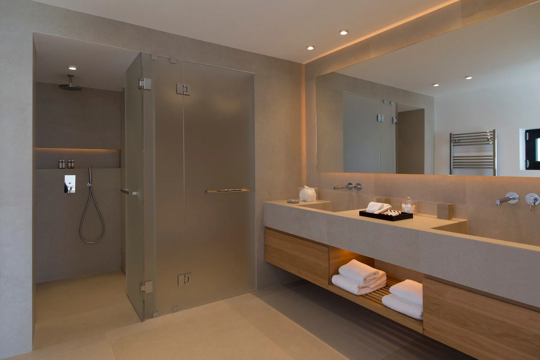 Un baño moderno con ducha y un largo lavabo.