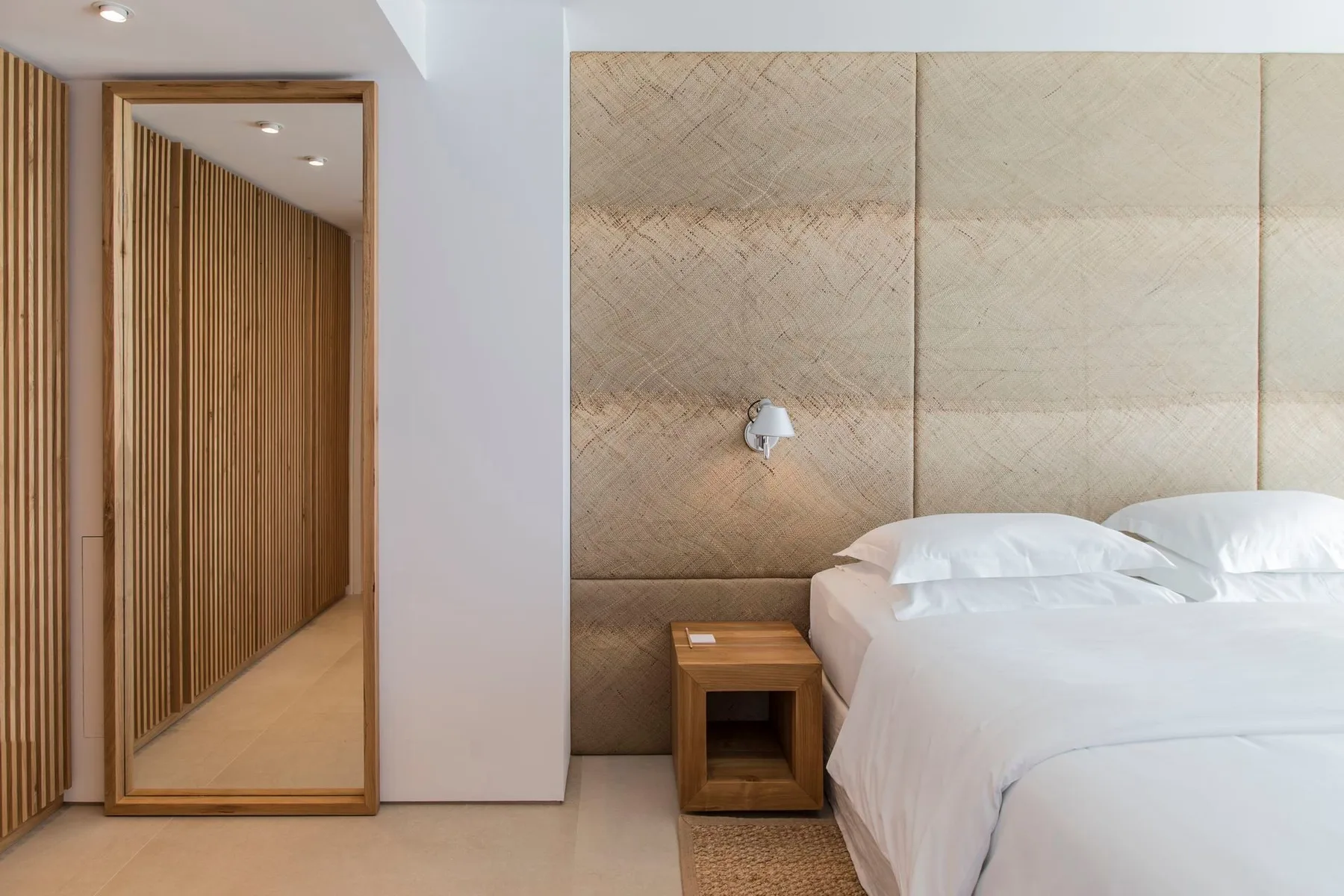 Un dormitorio con una cama blanca junto a un espejo de cuerpo entero y una pared de listones de madera.