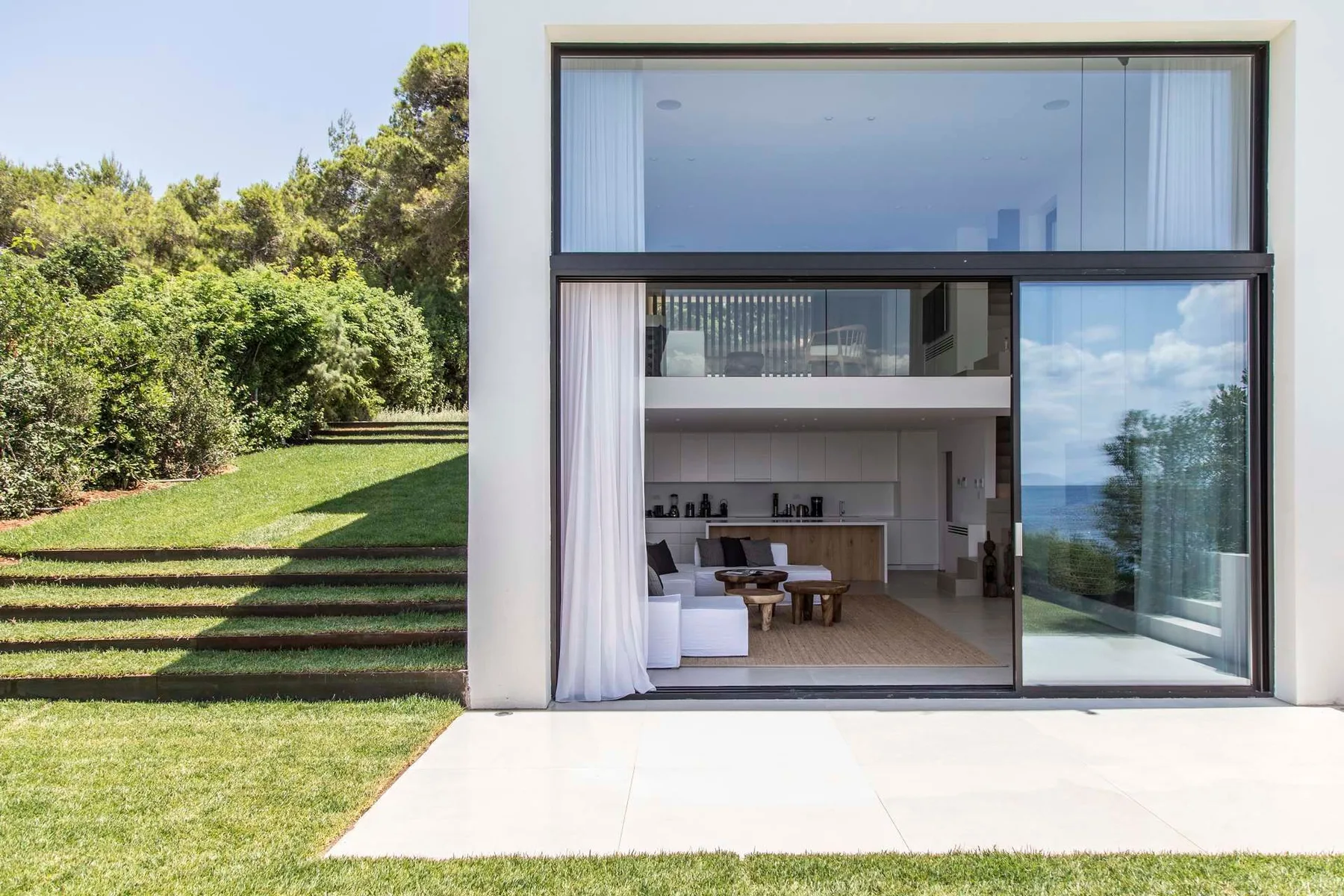 Casa moderna con una amplia abertura acristalada hacia el césped y los árboles.