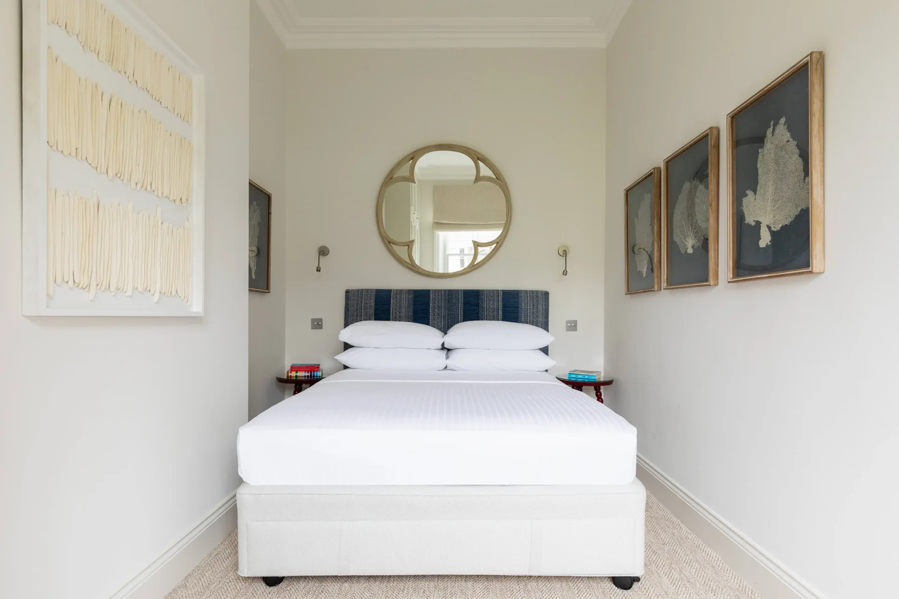 A bright bedroom with a neatly made bed and framed artwork on the walls.