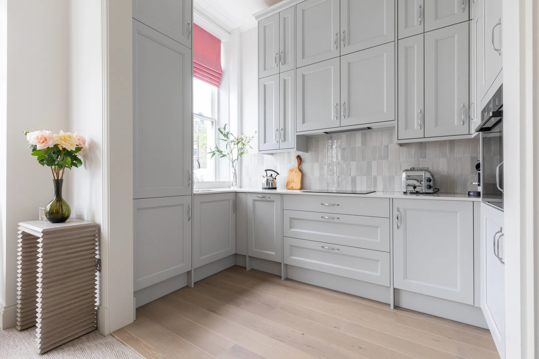 A bright kitchen with white cabinets, a window, and light wood flooring.