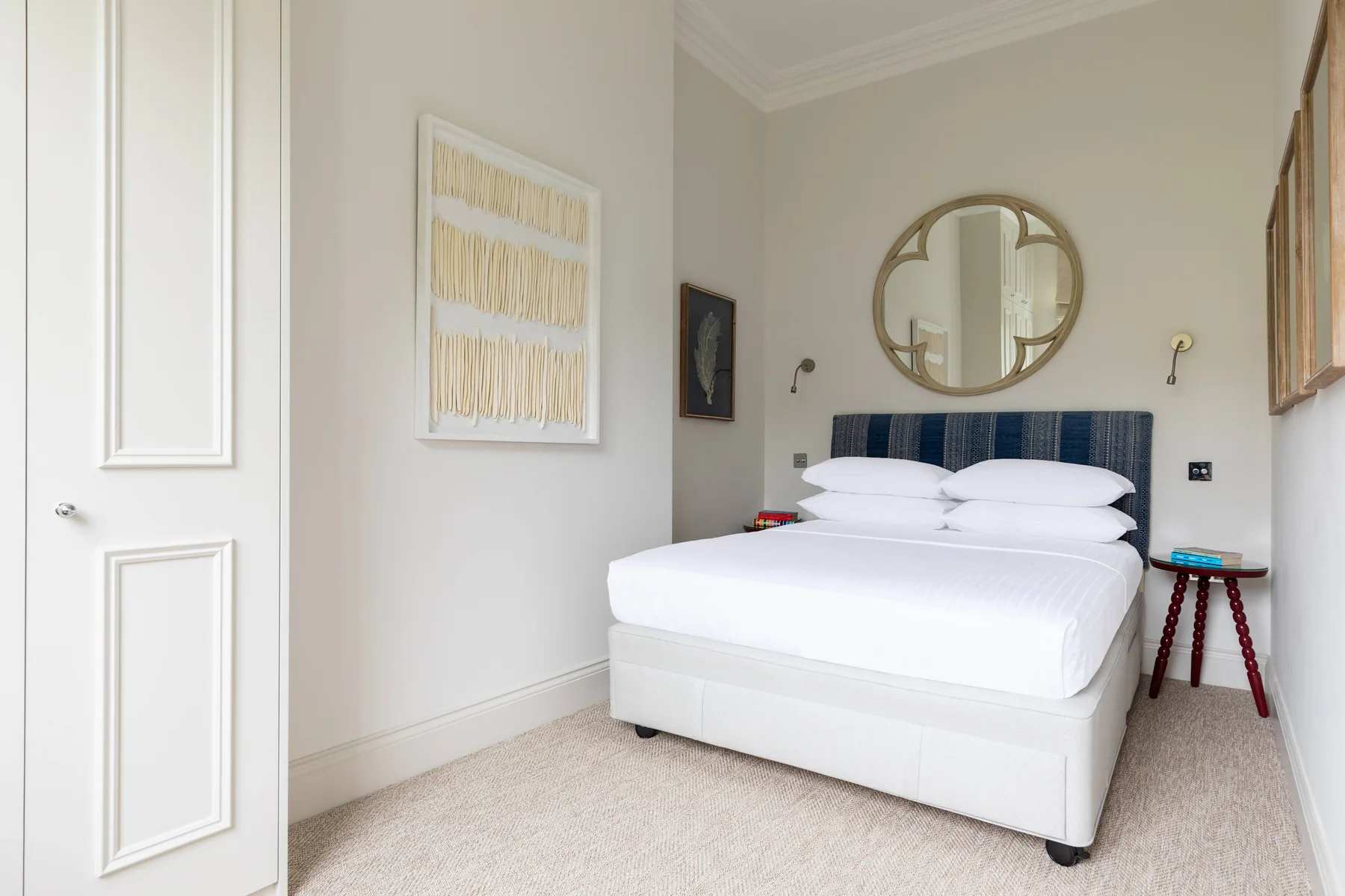 A bright bedroom with a neatly made bed and a round mirror above it.