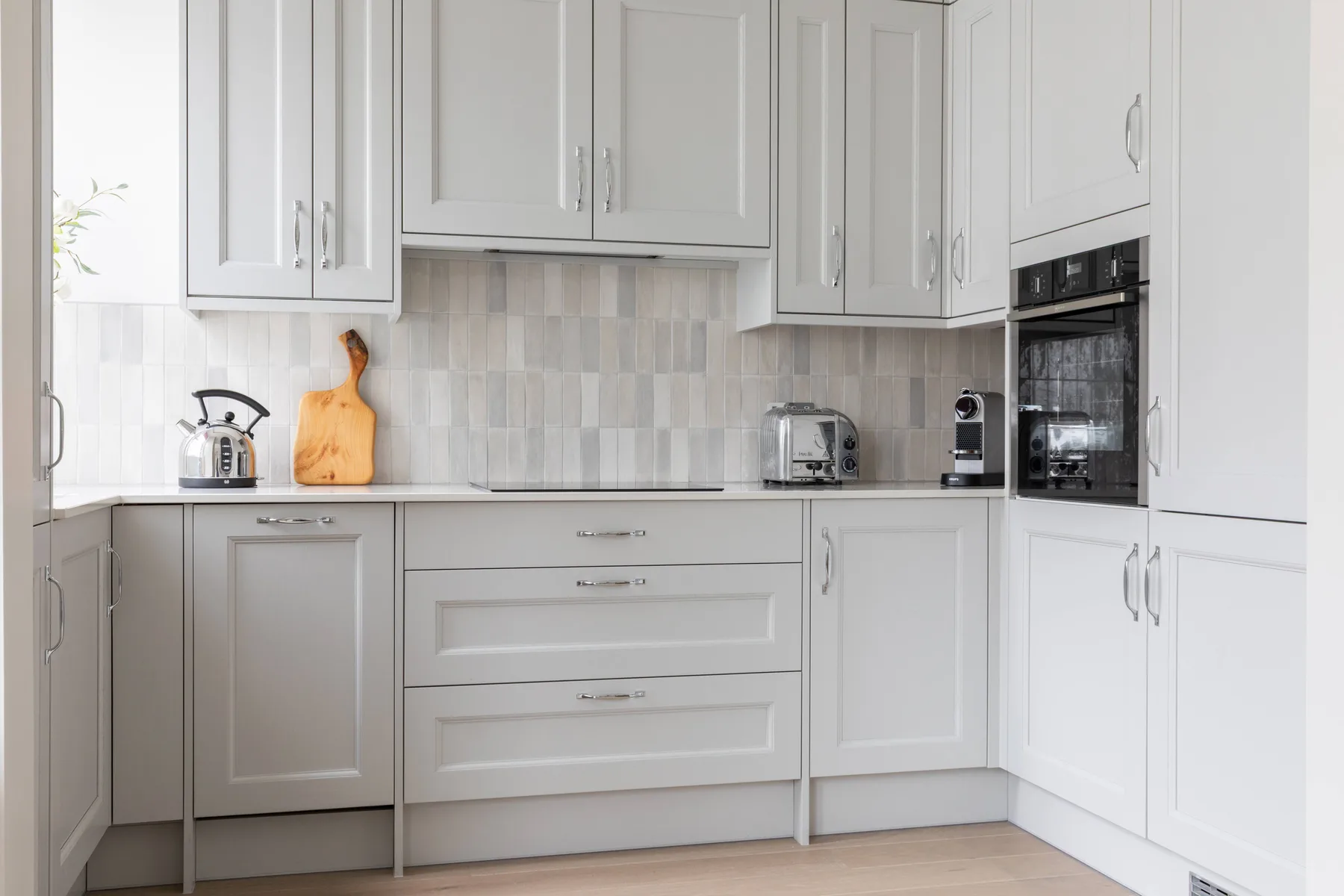 A bright kitchen with white cabinets, pale counters, and built-in appliances.