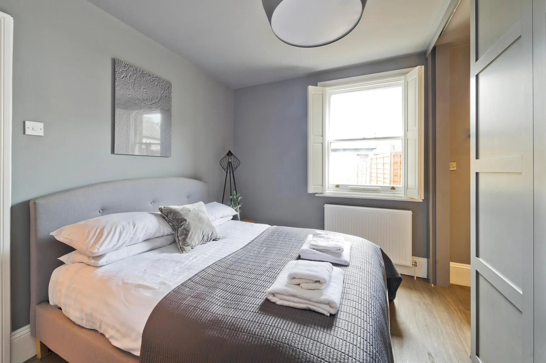 A bedroom with a neatly made bed and a window overlooking nearby buildings.