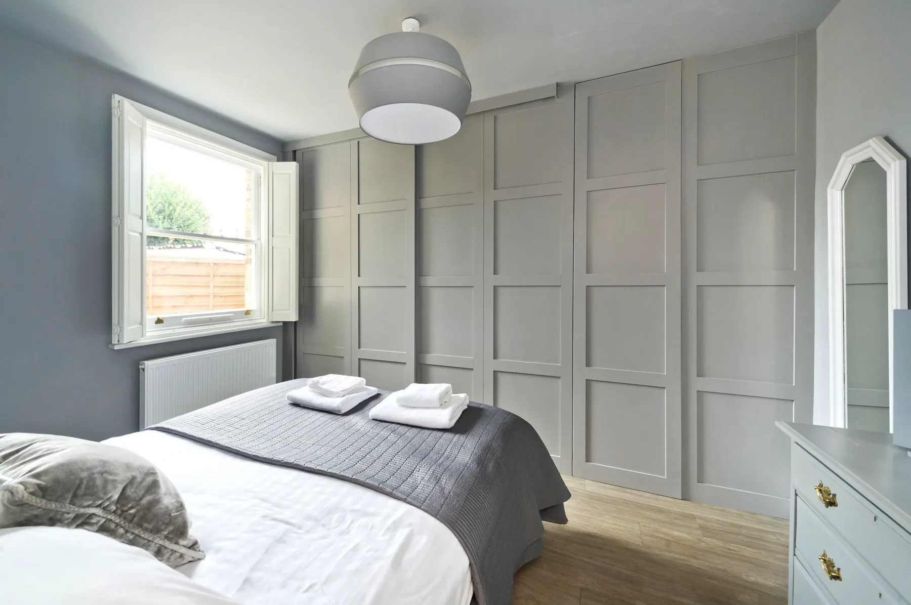 A bedroom with a bed, paneled walls, and a window.