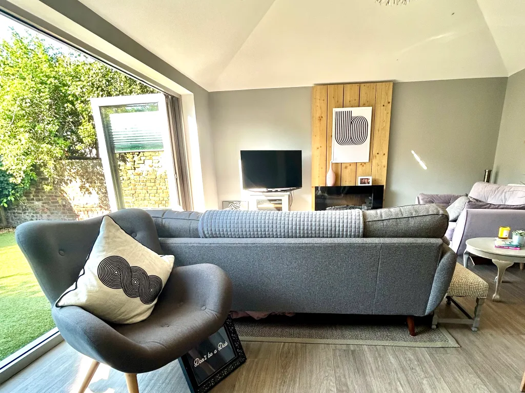 A bright living room with seating facing a television and large windows.
