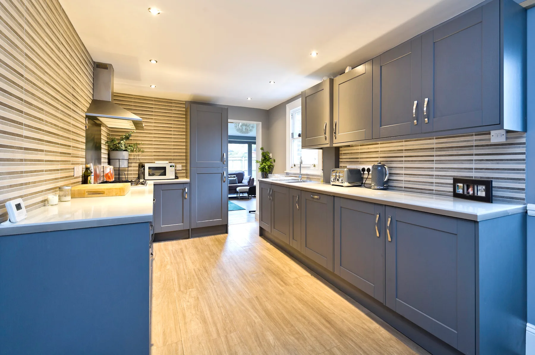 A modern kitchen with gray cabinets, light countertops, and a wood-look floor.