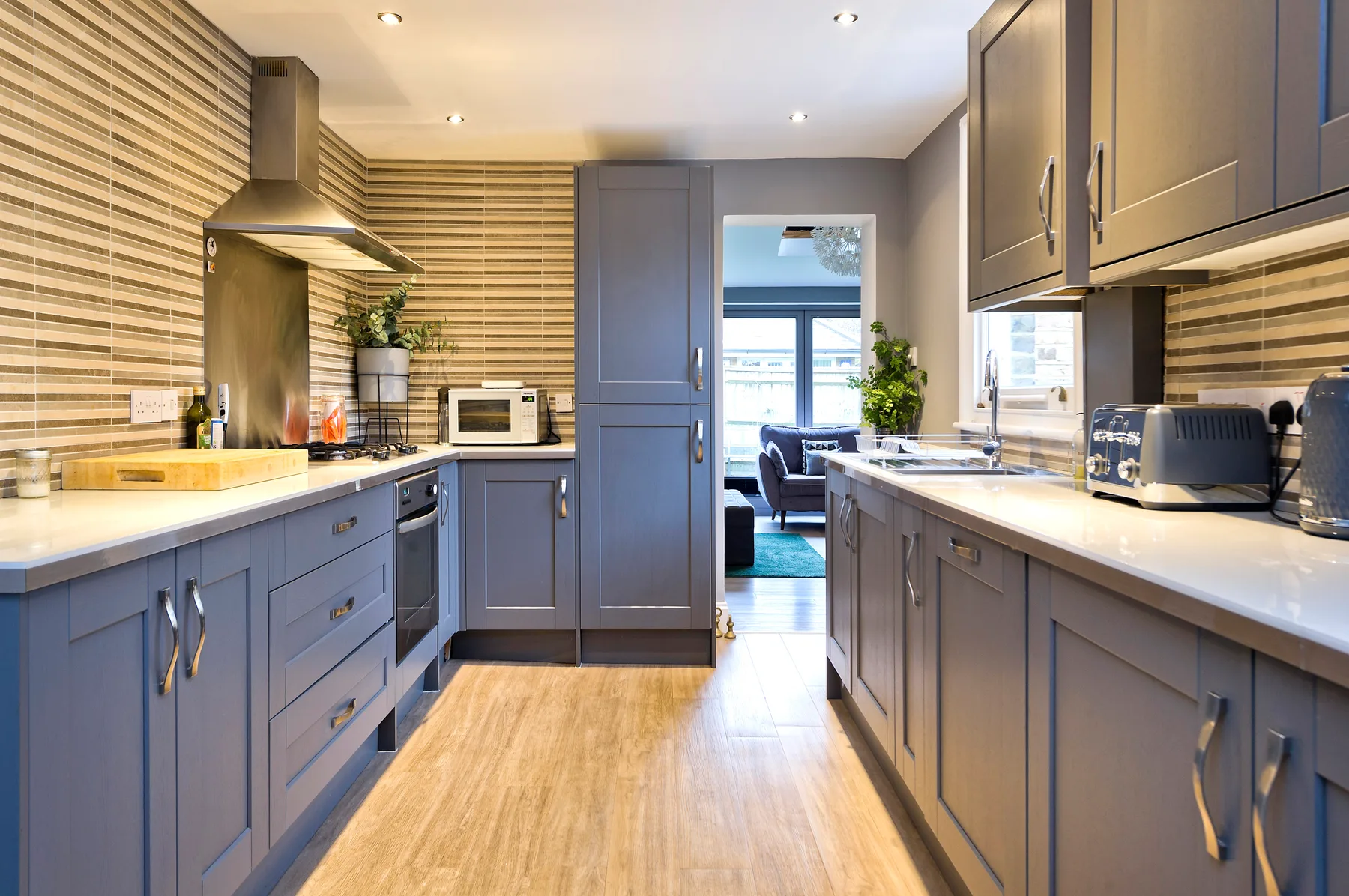 A modern kitchen with gray cabinetry, light countertops, and a doorway to the living area.