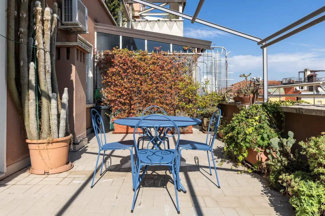 Una terraza en la azotea con un conjunto azul de comedor exterior y plantas en macetas.