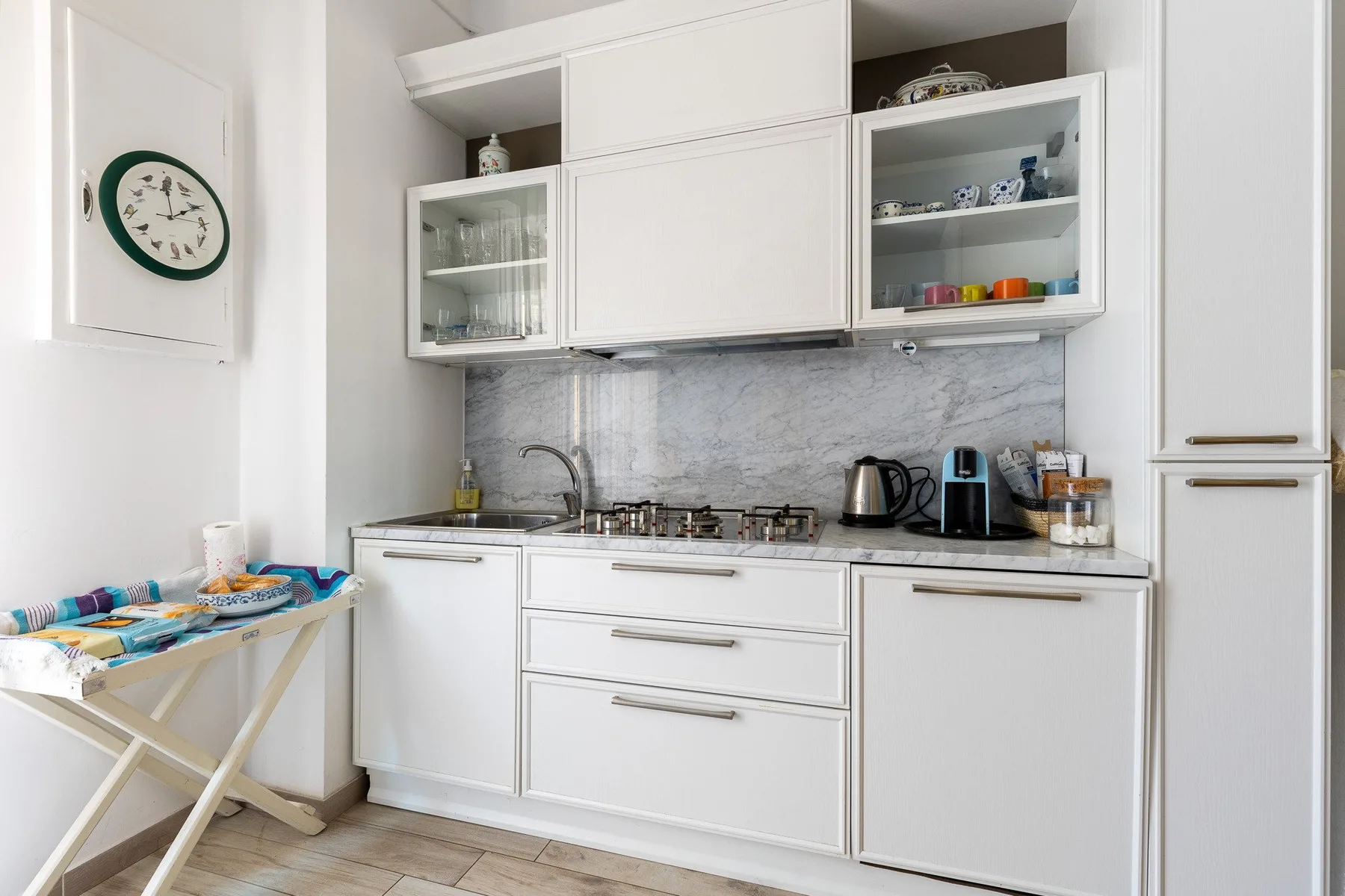 Una cocina blanca y luminosa con gabinetes, una placa de cocina y electrodomésticos sobre la encimera.