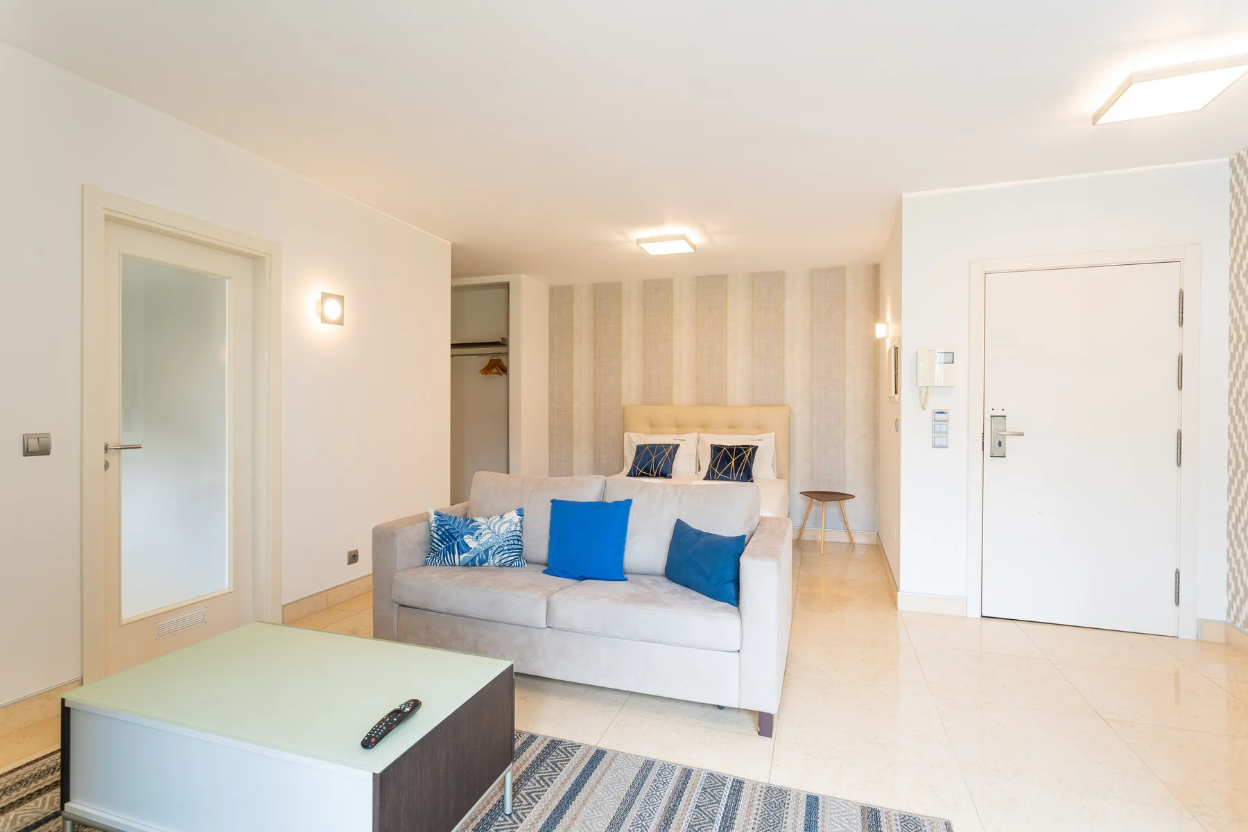 A bright studio room has a sofa, a bed, and a low coffee table.