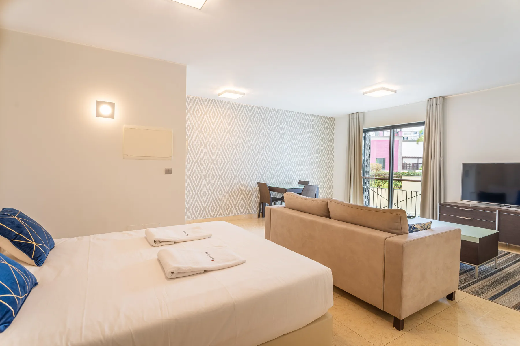 A studio room with a bed, seating area, and dining table.