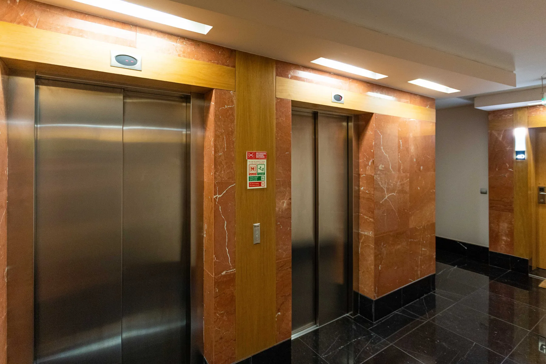 An elevator lobby with metal elevator doors and polished dark flooring.