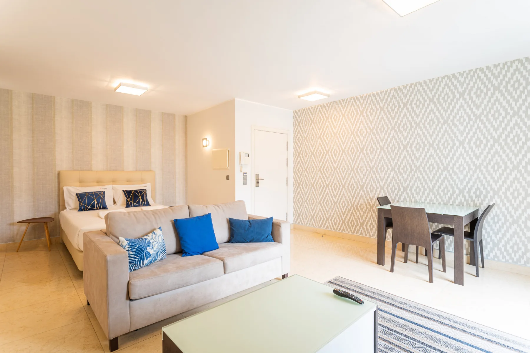 A bright living area with seating, a dining table, and patterned wallpaper.