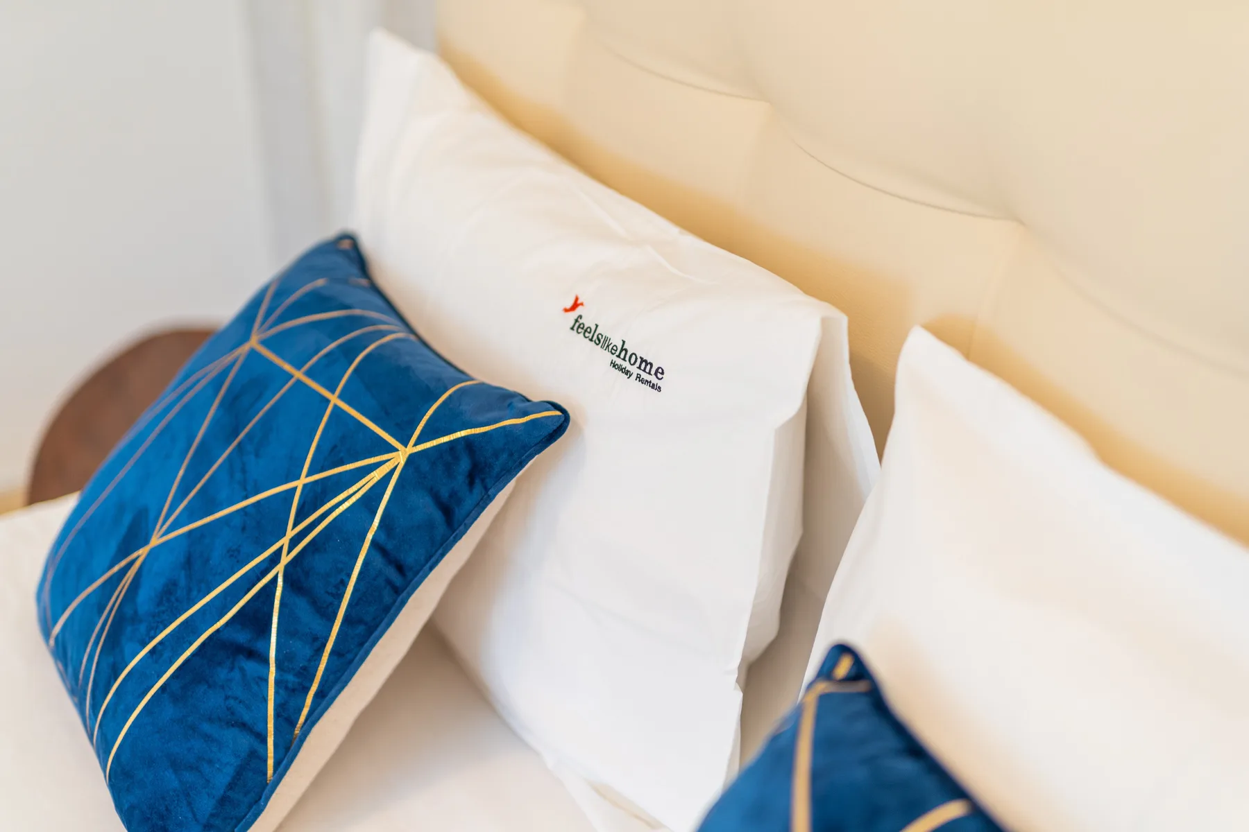A bed with white pillows and blue decorative cushions.