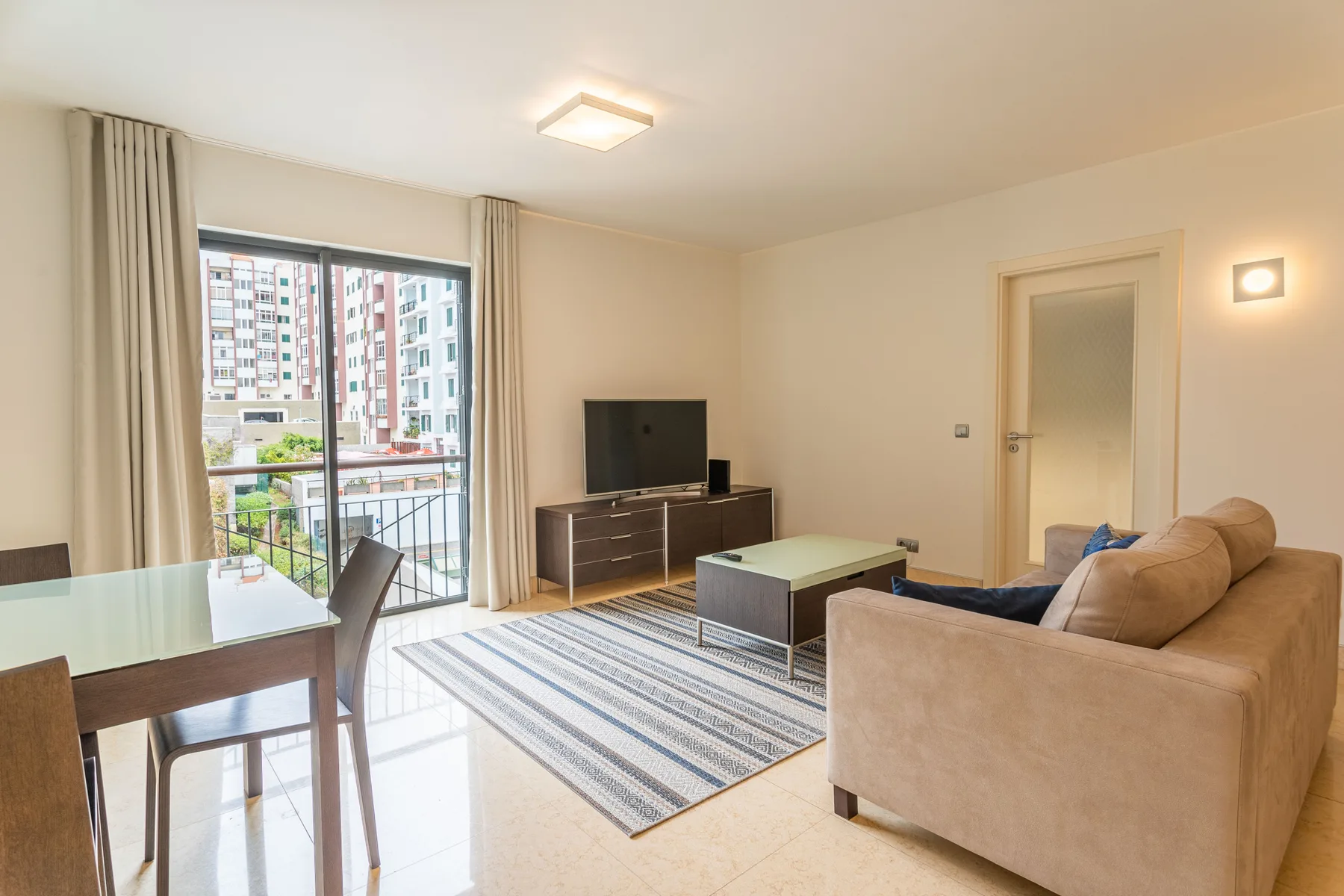 A bright living area with a dining table beside a balcony window.