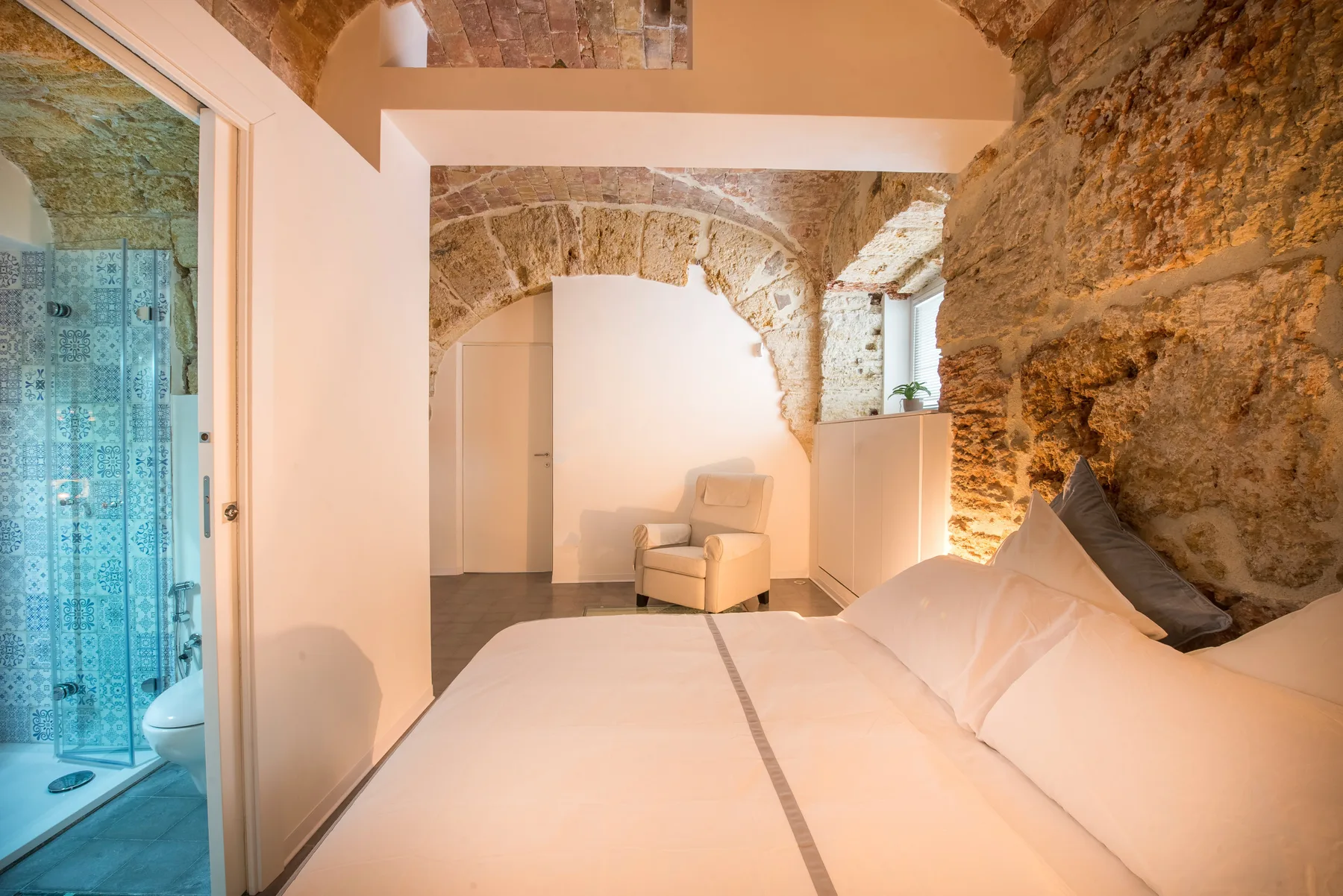 A bedroom with a large bed, exposed stone walls, and an adjoining bathroom.